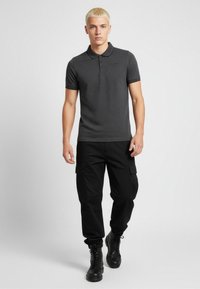 Camisa polo de carbón con cuello y mangas cortas, combinada con pantalones cargo negros y botas negras. Textura suave, diseño casual, sin patrones.