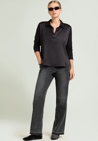 Polo a maniche lunghe nero con colletto, abbinato a jeans larghi e sbiaditi neri. Tessuto liscio con una sottile lucentezza; calzature casual.