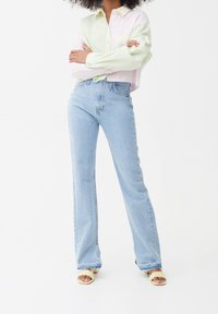 Jeans azzurri a vita alta con gamba dritta, dettagliati con orli sfilacciati, abbinati a una camicia button-up color pastello a blocchi di colore.