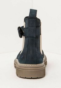 Botín de ante azul marino con un panel lateral beige, que presenta un detalle de hebilla, un acabado texturizado y una suela de goma flexible.