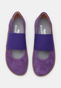 Zapatos de ante púrpura que presentan una amplia banda elástica púrpura en la parte media del pie, punta redondeada y suela plana. Plantilla Ortholite visible.