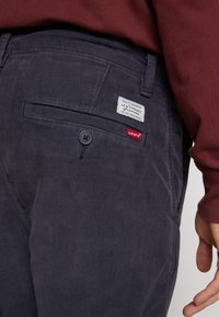 Marinblå kordflöjlsbyxor med en framknappning, sidofickor och Levi's-märke i vitt och rött på bakfickan.