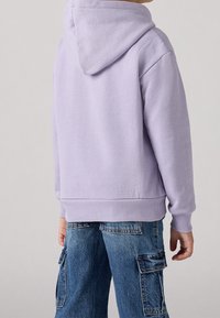 Sudadera con capucha lila, con un dobladillo y puños de canalé, que presenta una textura suave. Combinada con pantalones cargo de mezclilla que muestran bolsillos laterales.