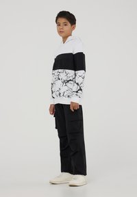 Felpa con cappuccio in bianco e nero con motivo marmo, dotata di polsini e orlo a costine. Abbinata a pantaloni cargo neri e sneakers bianche.