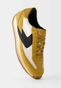 Sportiga sneakers med en överdel i gult mocka och vita detaljer, svart sidologotyp och gummisula i brunt. Snörningsdesign med vadderad krage.