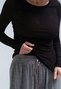 Schwarzes Langarmoberteil mit taillierter Passform, kombiniert mit grauen, strukturierten Hosen mit elastischem Bund und Satin-Zugbanddetails.