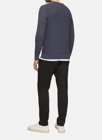 Marineblauer strukturierter Pullover mit Rundhalsausschnitt, kombiniert mit schwarzen Hosen und weißen Sneakern, zeigt eine lässige Rückansicht.