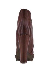 Zapato de tacón alto de cuero marrón con textura suave, punta redondeada y cortes curvados en los laterales, con un tacón grueso y suela clara.