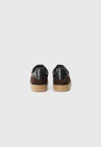 Sneakers in suede marrone con dettagli in pelle nera, colletto alto e suole in gomma sabbia. Vista posteriore che mostra il design a doppio materiale e le cuciture.