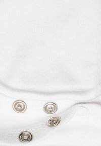 Body en coton blanc avec une texture douce, doté de quatre boutons-pression en argent sur le bas pour un passage facile.