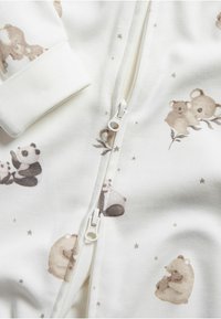 Valkoinen vetoketjullinen haalari, jossa on karhu- ja pandakuviot. Ominaisuuksiin kuuluu pehmeä kangas, elastiset hihansuut ja keskeinen vetoketju, jossa on pyöreä vetotanko.