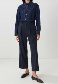 Marindeminskjorta med guldknappar, två bröstfickor; tillsammans med högmidjade mörka byxor med sidofickor och uppvikta fållar. Svarta ballerinas.