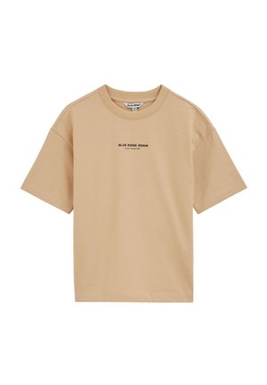 Smėlio spalvos trumpomis rankovėmis medvilninė palaidinė su apvalia iškirpte, ant krūtinės centre užrašytas tekstas „BLUE RIDGE DENIM STAY FEARLESS“, paprasto dizaino, matomas kaklo ženklas.