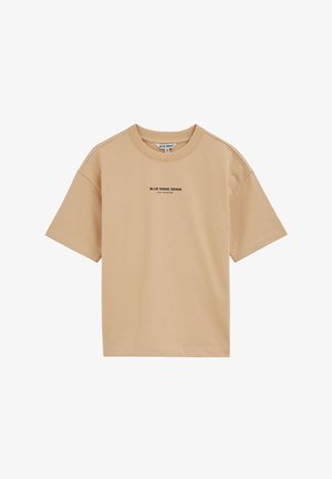 Beige T-shirt met korte mouwen en ronde hals met de tekst "BLUE RIDGE DENIM STAY FEARLESS" gecentreerd op de borst, eenvoudig ontwerp en zichtbare neklabel.