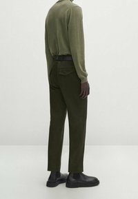 Olijfgroen longsleeve shirt met een ontspannen pasvorm, gecombineerd met donkergroene broeken. Een gladde textuur en zwarte schoenen maken de outfit compleet.
