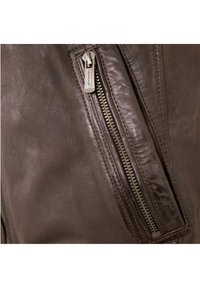 Braune Lederjacke mit einer seitlichen Reißverschlusstasche. Das Leder zeichnet sich durch eine glatte Textur und einen subtilen Glanz aus und zeigt eine detaillierte Nahtführung.