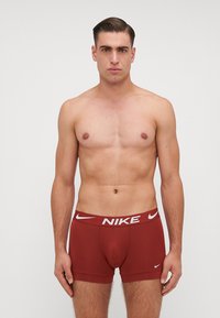 Boxeri scurți roșii Nike, cu un logo alb pe talie, având un design ajustat și o textură netedă a materialului. Fără modele sau accente suplimentare.
