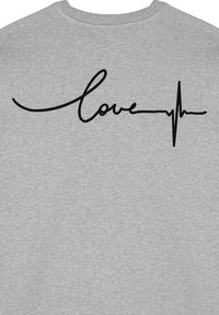 Felpa grigia con la parola "love" in un font corsivo nero, con una linea del battito cardiaco integrata nel testo. Texture morbida e liscia.