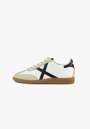 Tenisky s bielym koženým zvrškom, béžovými semišovými detailmi, čiernou koženou pätou a štruktúrovanou gumenou podrážkou. Majú biele šnúrky a krížový vzor.