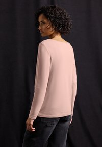 Helles rosa Langarmtop mit rundem Ausschnitt, gefertigt aus weichem Stoff. Besitzt einen lockeren Schnitt und nahtlose Schultern. Wird zu dunklen Jeans getragen.