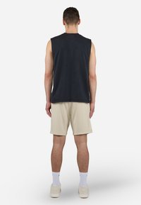 Top de algodón sin mangas de color gris oscuro combinado con pantalones cortos beige, con un ajuste relajado y un diseño minimalista; modelo mostrado de espaldas.