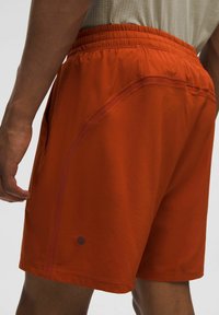 Herrers orange atletiska shorts med en stretchig midjeband, sidfickor och en diskret logotyp nära fållen. Slät, lättviktig väv.