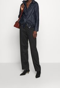 Marinblå vattentät jacka med justerbara dragsnören, två framfickor och silverfärgade dragkedjor, i kombination med svarta vida byxor och spetsiga ankelstövlar.