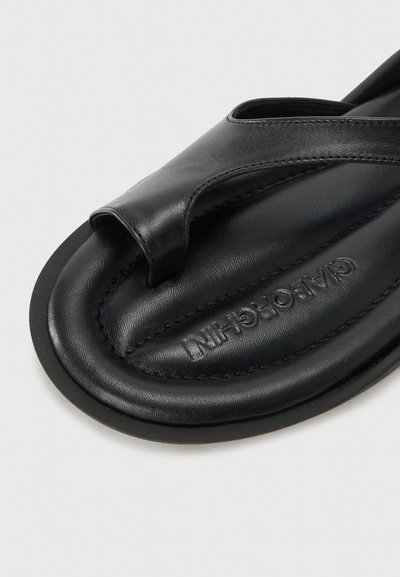 Musta nahkainen sandaali flip-flop, jossa on teksturoitu pohja, ristikkäinen hihnasuunnittelu ja kontrastiväriset ompeluseikat. Kumipohja pitävyyttä varten.
