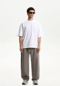 Witte oversized katoenen t-shirt gecombineerd met losse grijze sweatpants. Grijze sportschoenen met een gestreepte zool en een zwart zonnebril.