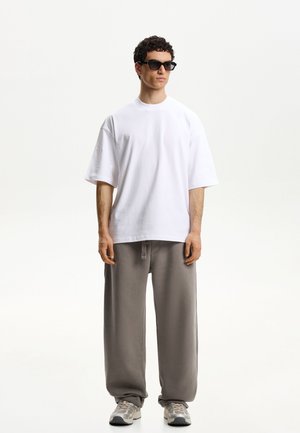 Hvid oversized bomulds t-shirt parret med løse grå sweatpants. Grå løbesko med et mønstret sål og sorte solbriller.