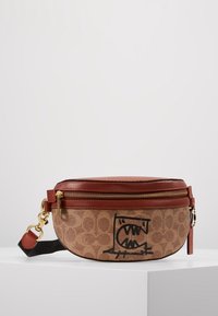 Mediumstor brun canvasväska med en läderöverdels, gulddragkedja och en svart grafisk design. Inkluderar ett avtagbart axelband och texturerad yta.