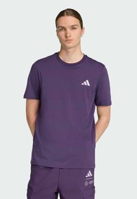 Paarse katoenen T-shirt met korte mouwen, ronde halslijn en een klein wit Adidas-logo op de borst. Soepele textuur, casual pasvorm.