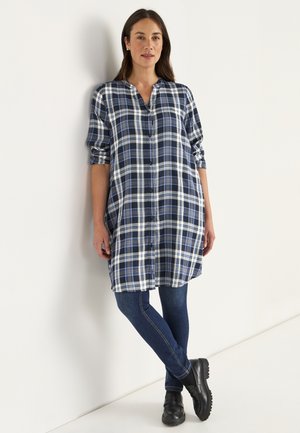 Langarm, knoopsluiting geruite shirt in marineblauw, wit en lichtblauw met een comfortabele pasvorm, gecombineerd met strakke donkere jeans en zwarte schoenen.