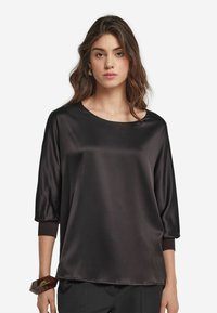 Svart satin topp med båtformad halsringning, trekvartslånga ärmar och uppvikta fållar. Slät textur med en avslappnad passform och minimala designdetaljer.