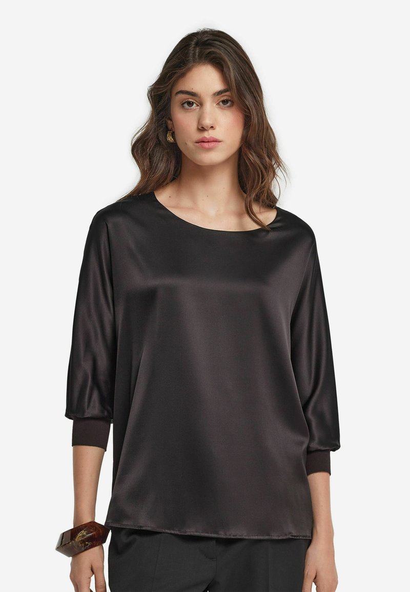 Svart satin topp med båtformad halsringning, trekvartslånga ärmar och uppvikta fållar. Slät textur med en avslappnad passform och minimala designdetaljer.