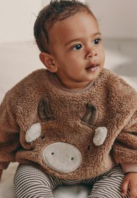 Brun fleece-tröja med motiv av en kos ansikte, med cremefärgade detaljer och texturerade öron. Matchas med randiga leggings. Mjuk och mysig look.