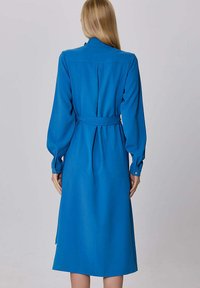 Robe à manches longues avec ceinture en tissu lisse et bleu vif. Dispose d'un col classique, de poignets boutonnés et d'une jupe fluide.