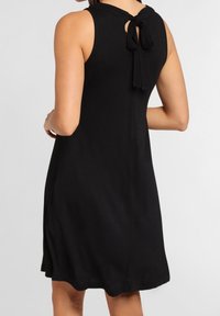 Sleeveless black knee-length dress with back bow tie detail worn by a person shown from behind.