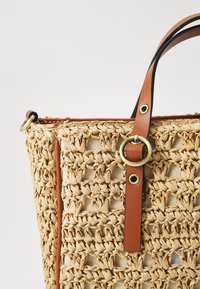 Geflochtene Strohtasche mit quadratischem Muster, Karamell-Lederakzenten und messingfarbener runder Hardware. Schulterriemen in Schwarz und Braun.
