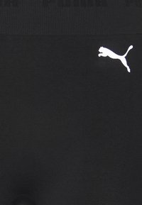 Černé legíny se strečovým, hladkým materiálem a horizontálně žebrovaným páskem v pase. Na boku je viditelné bílé logo Puma.