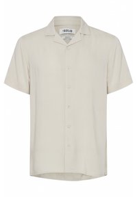 Kortermet, skjorte med knapper i lys beige stoff. Har krage med spiss fasong og en rett nederkant med en subtil merkevarelabel på siden.