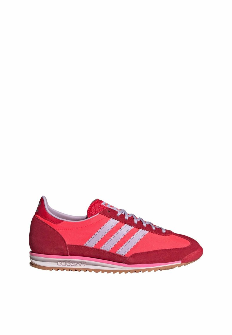 Zapatillas deportivas rojas con una combinación de texturas lisas y de gamuza, que presentan rayas blancas, punta redonda y una suela de color claro.