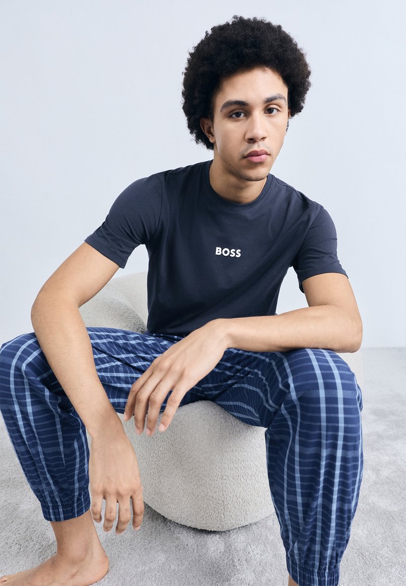 Tricou bleumarin din bumbac cu logo-ul "BOSS", asortat cu pantaloni de pijama în carouri albastre. Material moale, croială lejeră și manșete elastice vizibile.