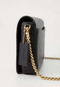 Geantă de umăr din piele neagră, cu un finisaj texturat, accesorii aurii, închidere cu fermoar și curea din lanț. Prezintă un tag atașat cu brandul.