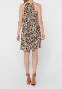 Robe beige à col licou avec motif cachemire noir, coupe ample et dos froncé. Portée avec des bottines à talons marron à bride cheville.