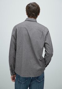 Grijze lange mouw shirt met een reguliere kraag, gestructureerde stof en knoopmanchetten. Achteraanzicht toont een rechte zoom en minimale details.