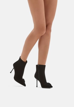 Stivali neri alla caviglia in morbido suede, con punta affusolata e un accent decorative, dotati di zip laterale e di un sottile tacco a stiletto.