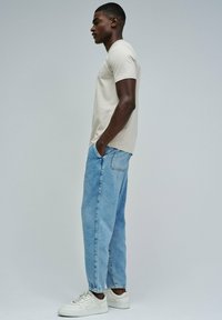 Camiseta de manga corta beige, jeans de mezclilla azul claro de corte suelto y zapatillas blancas. Diseño simple y minimalista con un aspecto casual.