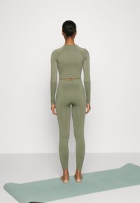 Olivgrön idrottstopp med långa ärmar och matchande högmidjade leggings, slät textur, åtsittande design, uppvisad mot en neutral bakgrund.