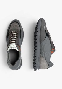 Zapatillas deportivas grises con una combinación de materiales de malla y ante, con acentos marrones, suelas texturizadas y cordones oscuros, vistas desde arriba y de lado.